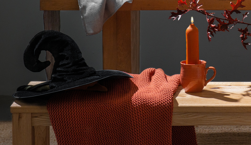 На фото товары Tkano: плед жемчужной вязки Essential и декоративная свеча оранжевого цвета Edge.